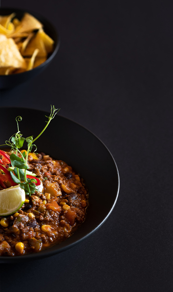 Zwei schwarze Teller auf schwarzem Hintergrund mit Tortillachips und Dipp